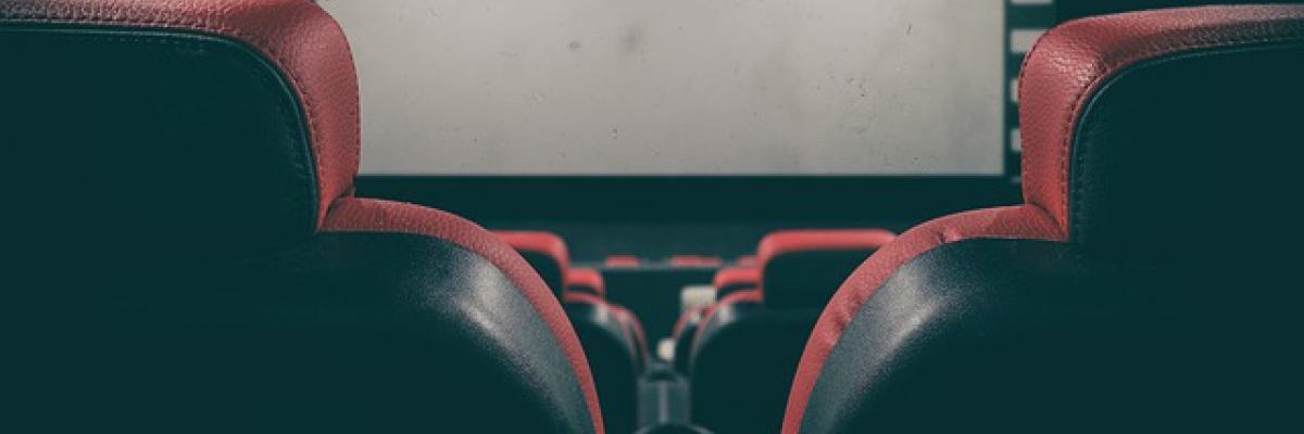 Une salle de cinéma vide. Des rangées de chaises sont empilées devant un écran sombre. 