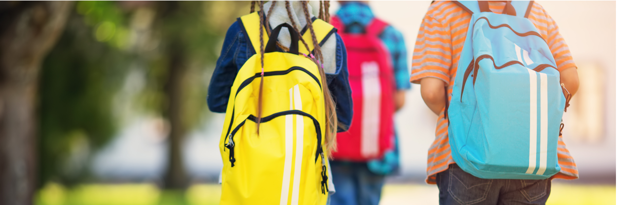Trois jeunes de dos se rendant à l'école. Ils portent des sacs à dos et sont à l'extérieur.