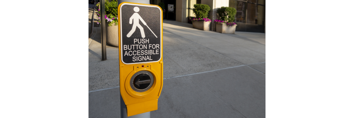 Un bouton-poussoir jaune/noir de signal d'accessibilité pour piétons sur un poteau.