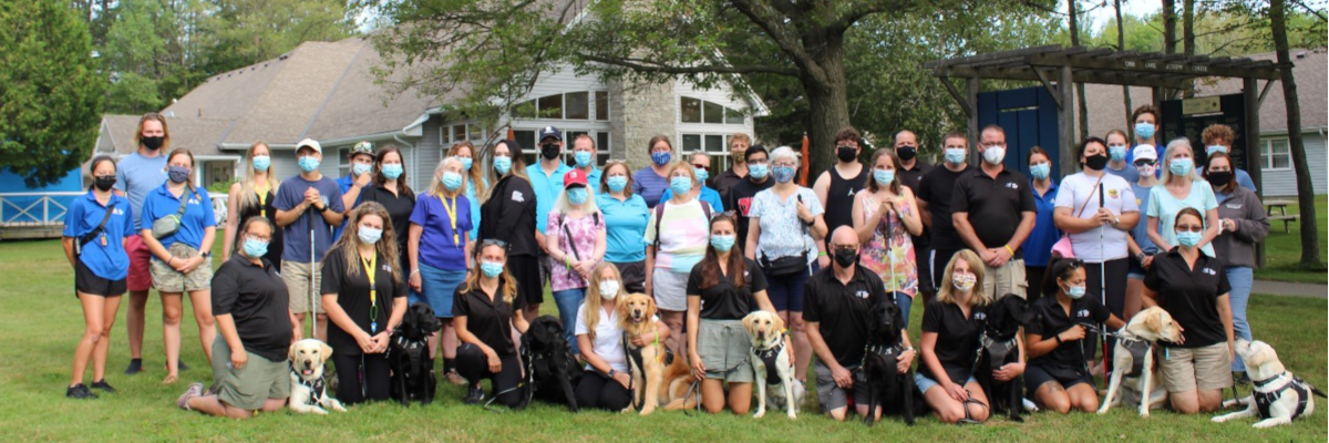 Les participants, le personnel de Réadaptation en déficience visuelle Canada, des Services communautaires Surdicécité et d’INCA, ainsi que les chiens-guides posant ensemble sur la pelouse du camp Lake Joe d’INCA