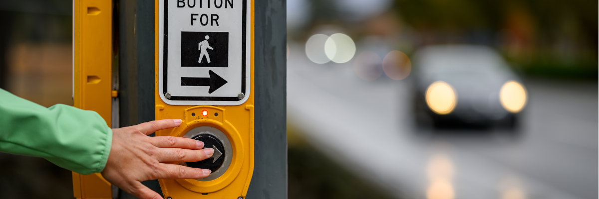 Une main appuie sur un bouton de passerelle pour piétons en attente de traverser une intersection.