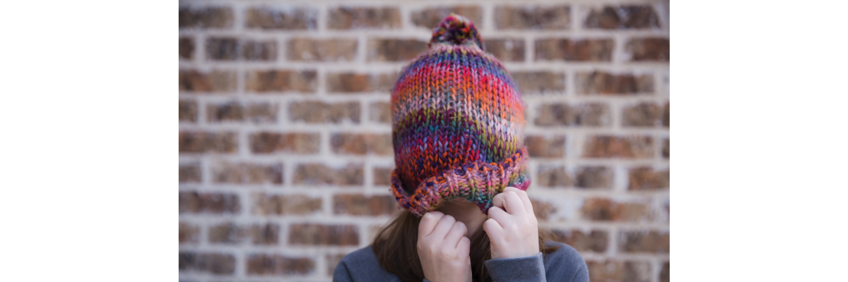 A young girl pulls her colourful winter hat over her face.