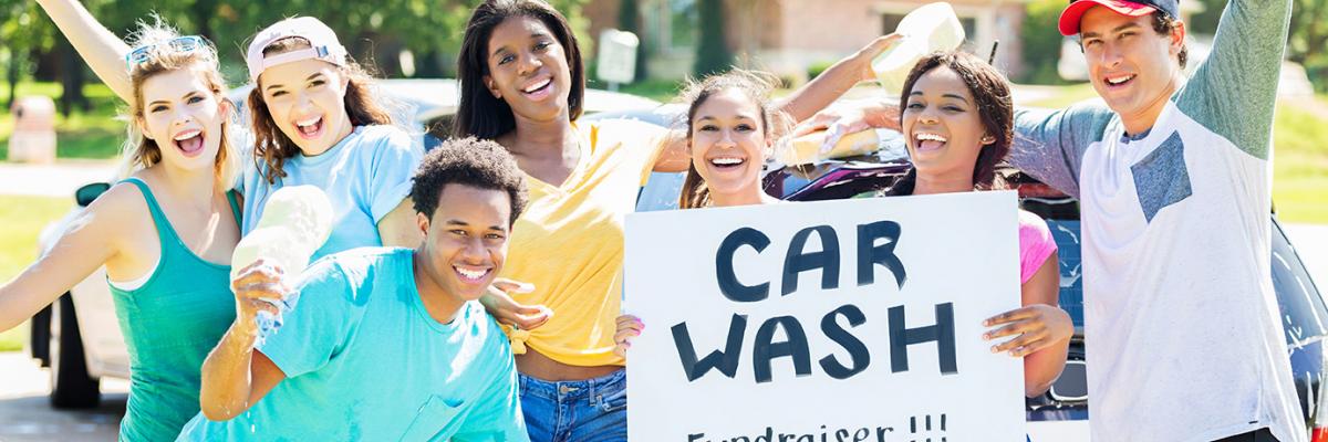 Group of individuals cheering with car wash sign