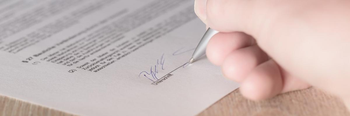 A woman's hand is shown signing a contract.