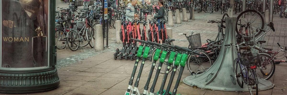  A city sidewalk with a row of electric scooters lined up on it.