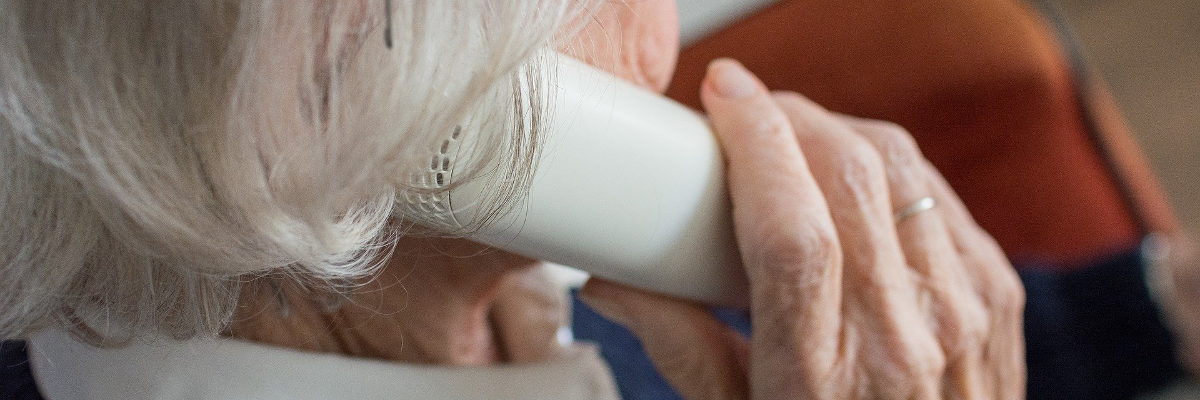 An elderly woman holds a landline telephone to her ear. 