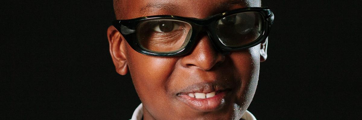 A young boy smiles for a school photo. He is wearing glasses and a polo shirt.