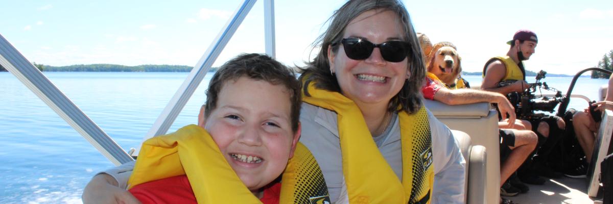 "A smiling  boy and a woman in life jacket sitting on boat deck"