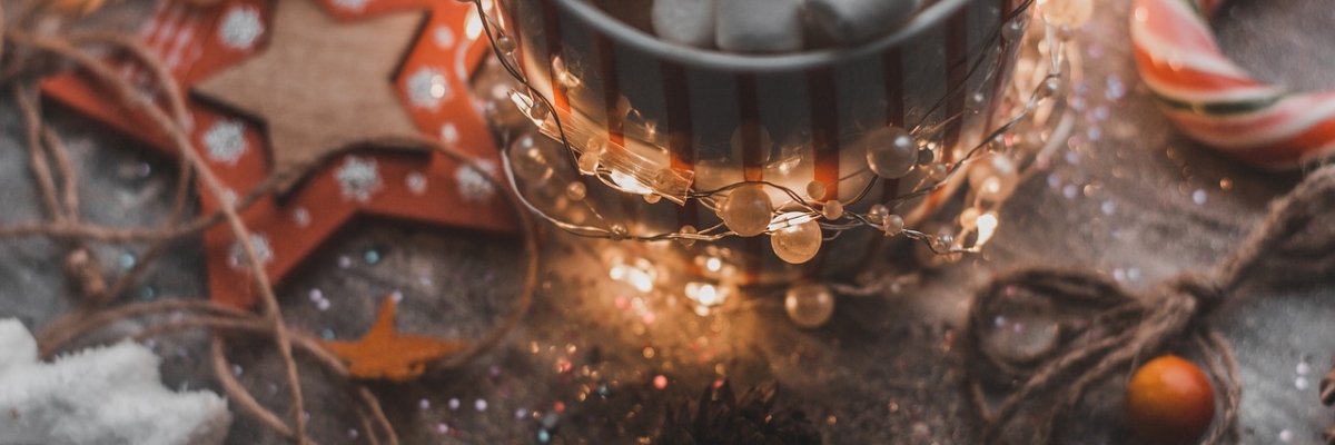 a mug filled with mini marshmallows is on a wooden table with candy canes, wooden ornaments, and tiny white lights.