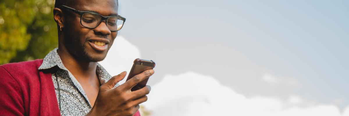 Un homme regardant la cellulaire dans sa main est dehors sous un ciel bleu et partiellement nuageux 