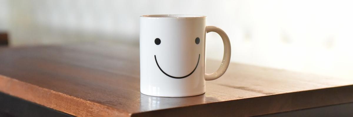 White mug sitting on a wood table. The mug has a smiley face on it.