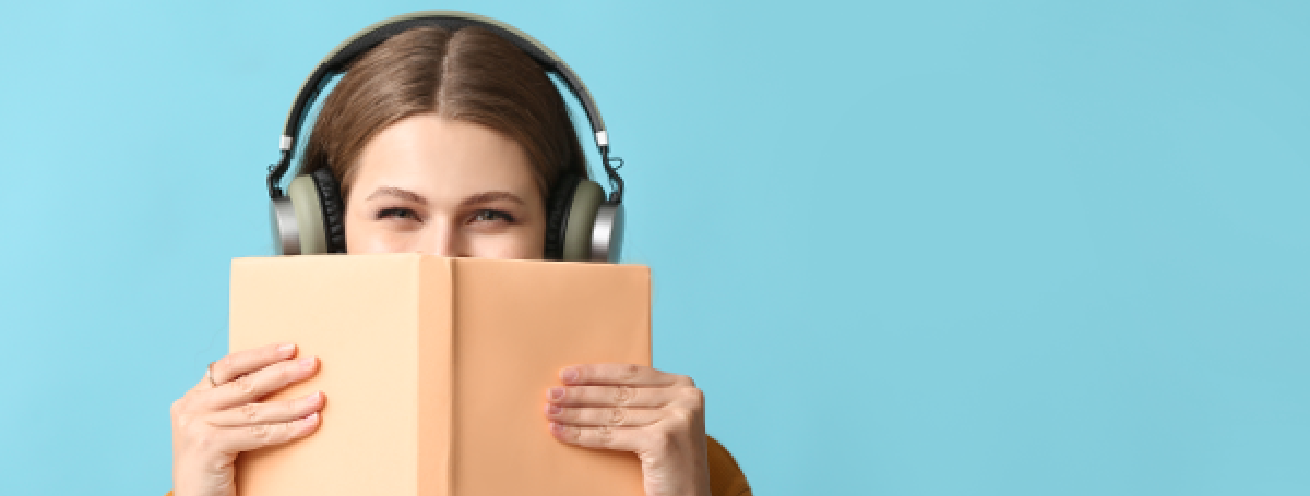 Une femme tient un livre devant son visage et porte des écouteurs.