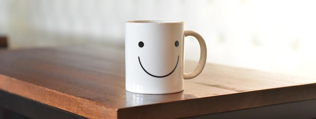 White mug sitting on a wood table. The mug has a smiley face on it.