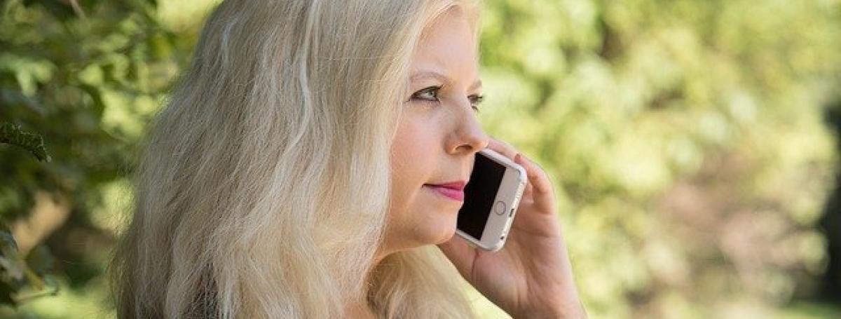 A woman holds an iPhone to her ear and listens intently to a private conversation.