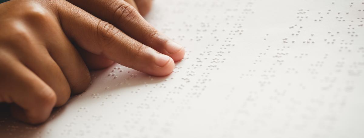 A young child's hands read a braille document.
