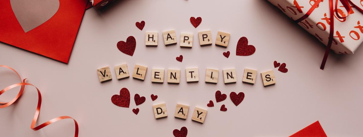 Valentine's day cards and gifts with the "Happy Valentines Day" written out with scrabble pieces and red hearts sprinkled.