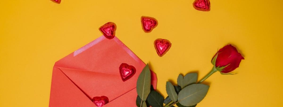 A red envelope with a red rose on top and red heart-shaped candies