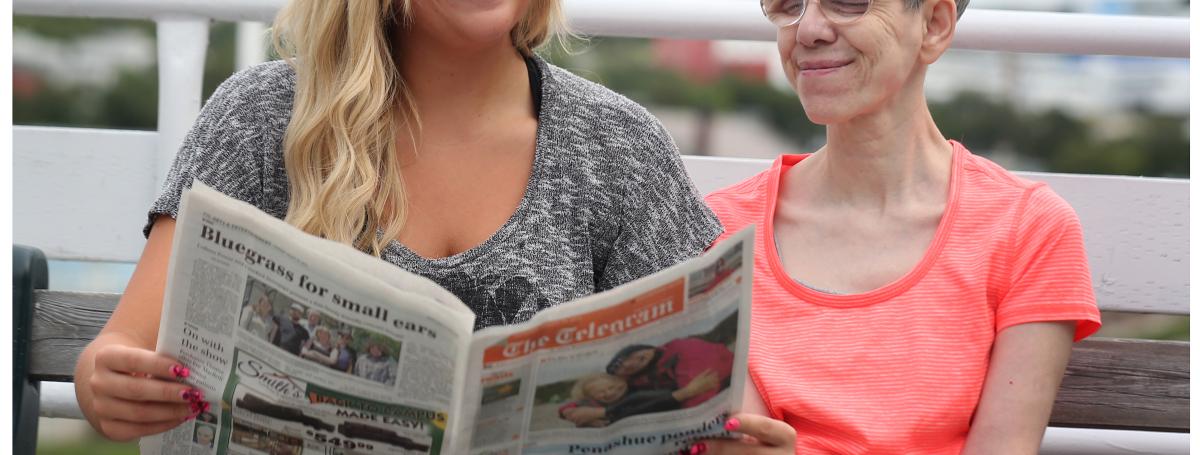 a young woman reads a newspaper to an older woman. 