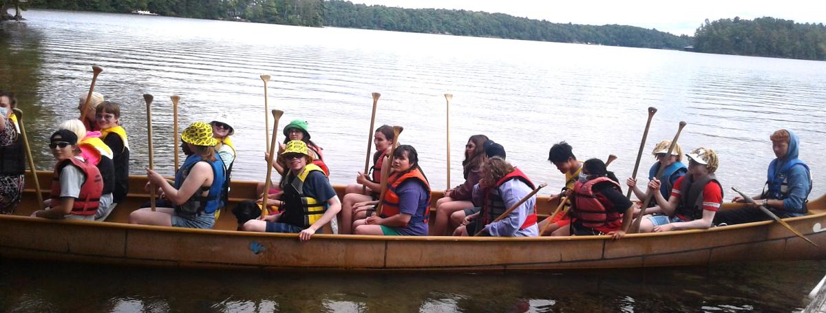 Youth have filled all the seats in the Voyageur canoe and are pushing off from the dock.