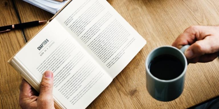 close up of hands holding a book and a coffee cup