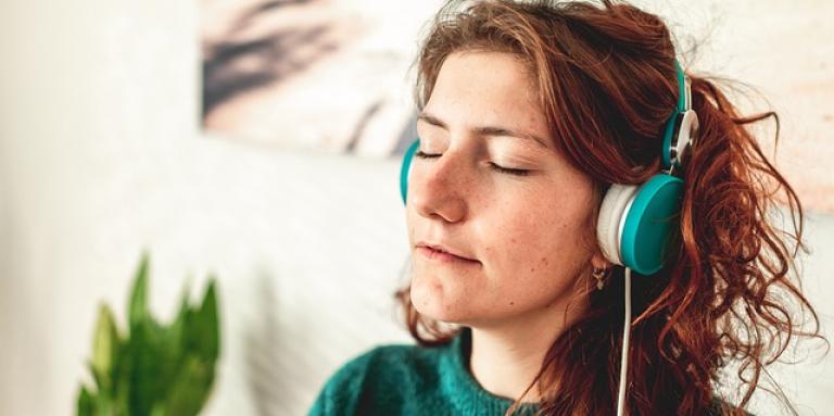 A young woman wears a pair of headphones and closes her eyes while listening to music.