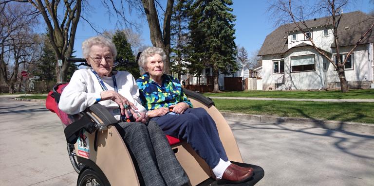 Two elderly women sit in a Cycles Toussaint Ami cruiser. 