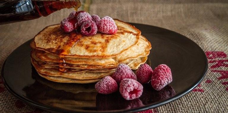A stack of pancakes with maple syrup and raspberries. 
