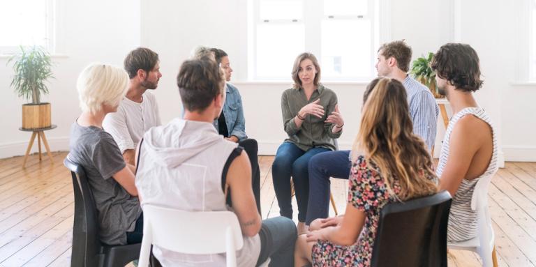 A group of 10 people sit in a circle and engage in lively conversation. 