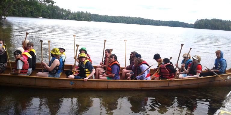 Youth have filled all the seats in the Voyageur canoe and are pushing off from the dock.