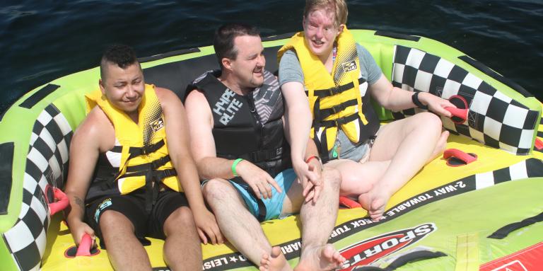 Three men in a colourful water tube on the lake