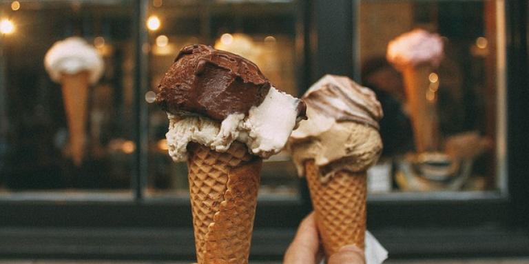Two waffle ice cream cones are held up in the air, side-by-side. 