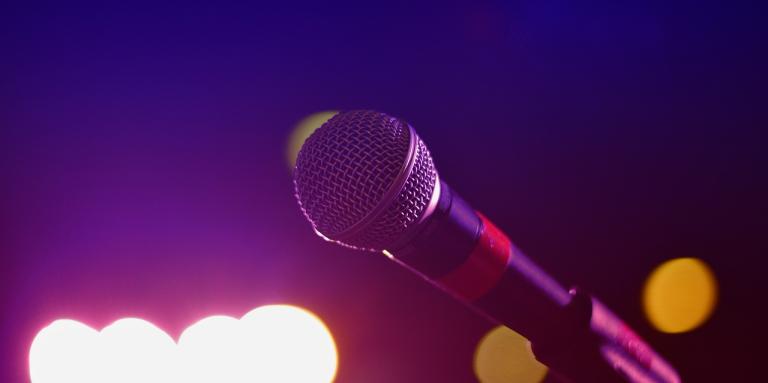 A microphone in a stand glimmers with stage lights in the background.