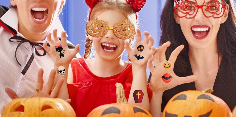 A man, girl, and woman are wearing Halloween glasses and hat, with halloween stickers on their hands.