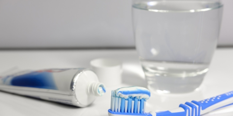 A toothbrush covered in toothpaste, a glass of water, and a tube of toothpaste are displayed on top of a bathroom sink.