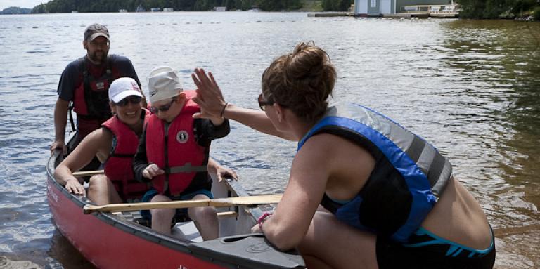 a group of campers in a canoe. one high fives a camp lead. 