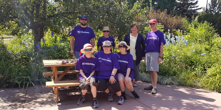 Group of volunteers wearing purple shirts stand smiling in a garden.