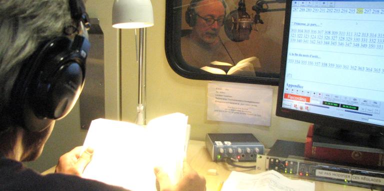A volunteer reader and technician record an audio book in a recording booth.