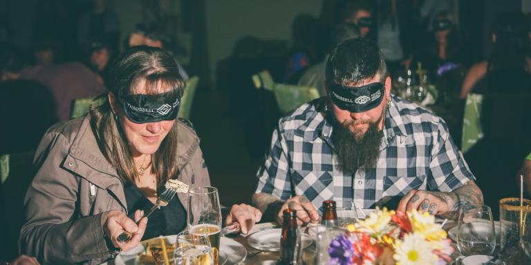 Two diners enjoying a meal with blindfolds on. 