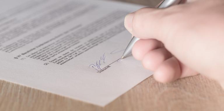 La main d'une femme est montrée en train de signer un contrat.