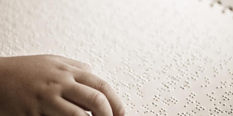 A hand on a book reading braille.