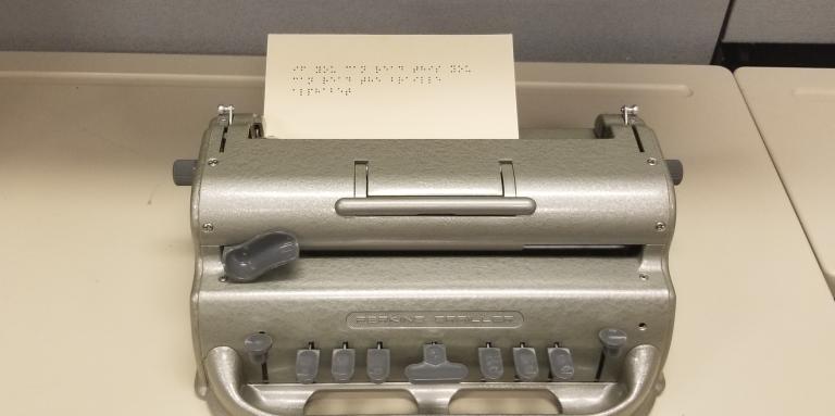Perkins Brailler with braille message on paper saying "if you can read this you can read the braille alphabet"