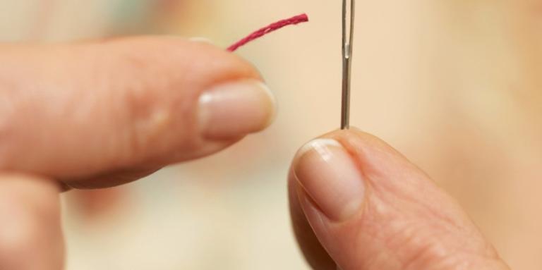 Close-up of person's fingers threading a small needle 