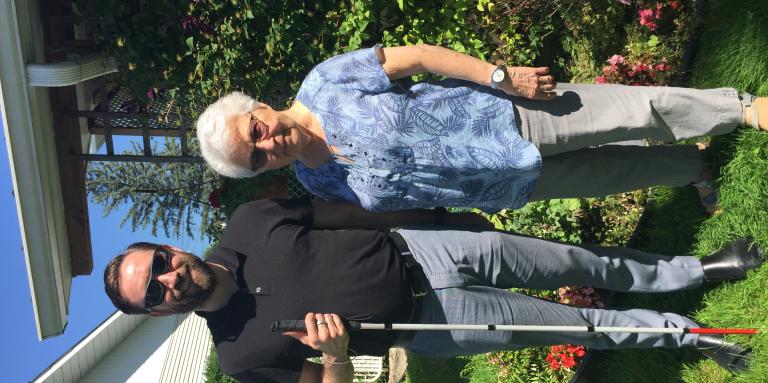 David Demers, Ed of Quebec CNIB Foundation with is white cane, next to Mrs Smith in her garden.