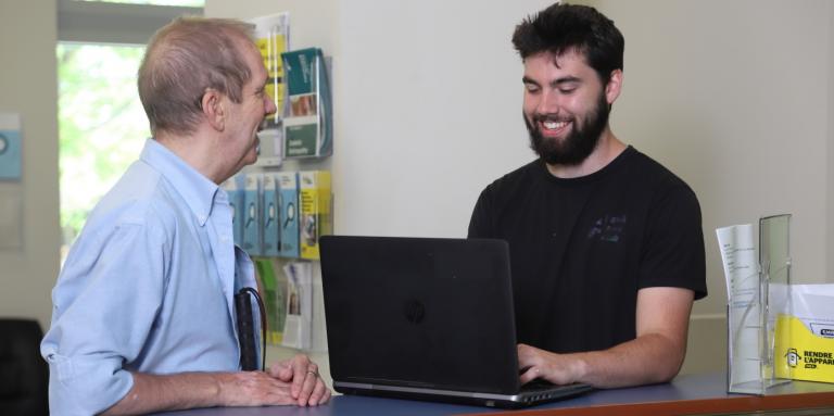 A CNIB volunteer and participant smile as they work together on a laptop