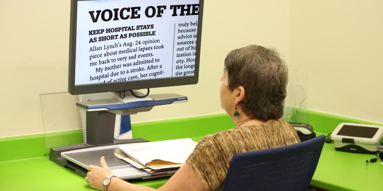 A woman sits at a CCTV and reads an enlarged document displayed on the screen.