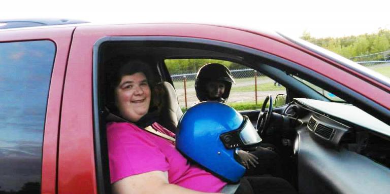 Julie Morneault assise dans un camion rouge avec un casque de moto bleu sur les genoux. Un dessin de cœur apparaît dans le ciel.