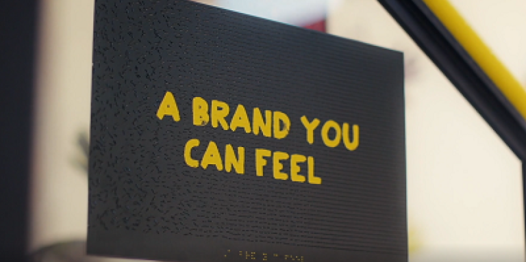 An image of a sign in braille with overlaid yellow CNIB branded letters in English reading A Brand You Can Feel