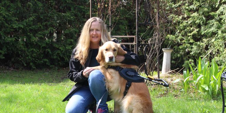 Diane Bergeron kneeling on grass next to her guide dog Carla, a golden retriever.