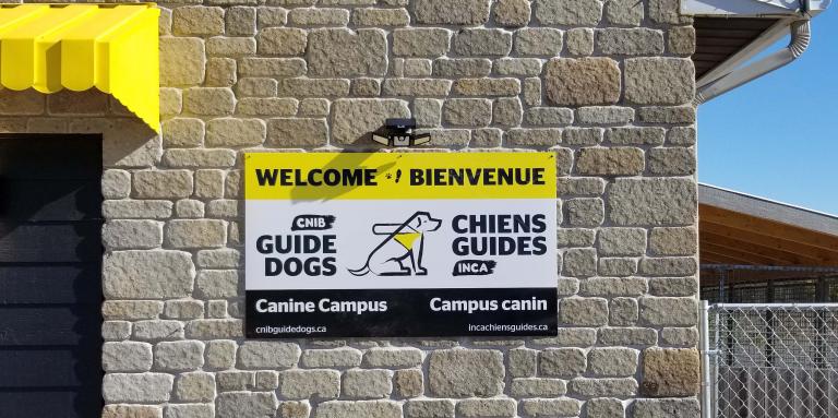 A photo of the welcome sign placed on the exterior of the Canine Campus. It reads: “Welcome & Bienvenue” with the CNIB Guide Dogs logo in the middle of the sign.