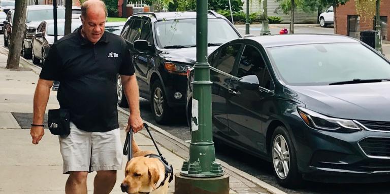Carl walking down a sidewalk with a CNIB Guide Dog in training.